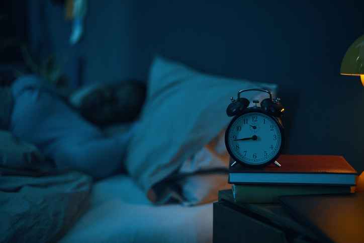 Person sleeping in bed with focus on alarm clock on nightstand - why do brain injury patients sleep so much