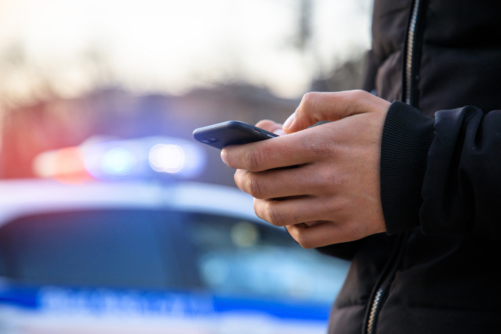 person holding phone next to a police car - Do you have to call the police for a car accident?